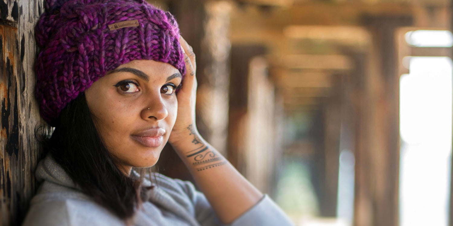Photo of a woman looking into the camera, modeling one of Baabushka's handmade merino wool scarves.